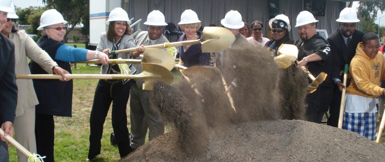 Group wearing white hard hats and shovelling dirt
